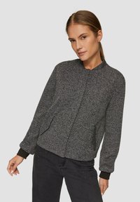 Blouson bomber en noir et blanc en motif pied-de-poule, avec des poignets et un col côtelés, comportant des poches latérales et une texture lisse.