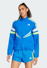 Chaqueta deportiva azul con acentos en blanco y verde neón, cierre de cremallera al frente, puños elásticos y pantalones cortos a juego. Presenta un logo en el pecho y un diseño elegante.
