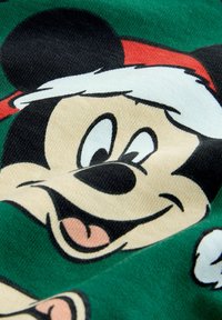 Grafika Myszki Mickey na zielonym materiale; zawiera czarno-białe detale, czerwony czapek Świętego Mikołaja oraz figlarny wyraz twarzy.