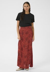 Maxi rok in het rood met een zwart dierenprintontwerp, met een hoge split. Gecombineerd met een eenvoudige zwarte t-shirt en beige schoenen.