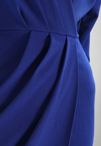 Tejido azul royal con pliegues drapeados, textura suave y diseño fluido. Sin hardware ni adornos visibles.