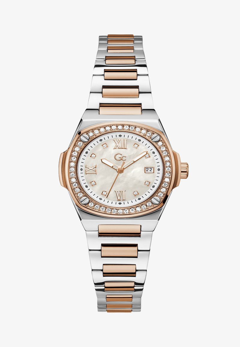 Ezüst és rose gold színű óra kerek tokban, gyöngyház számlappal, gyémánt díszítésekkel és lánckarkötővel. Római számokkal és dátumkijelzővel rendelkezik.