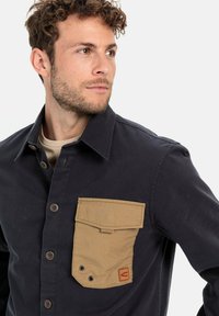 Overhemd met knopen in marineblauwe stof, met een tan corduroy zak; beschikt over een flap sluiting en logodetail, gestructureerde kraag en een gladde textuur.
