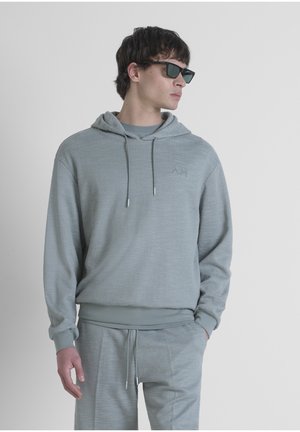 Sudadera gris claro hecha de material texturizado con capucha ajustable, puños acanalados y un sutil logo en el pecho; combinada con pantalones a juego.