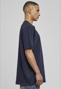 Tricou din bumbac de culoare bleumarin, cu mâneci scurte, croi lejer, gât rotund și detalii de cusătură vizibile, prezentat pe un model din lateral.