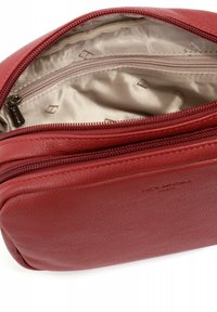Borsa in pelle rossa con una texture liscia, dotata di un compartimento con zip e rivestimento interno in satin beige con un sottile motivo del logo.