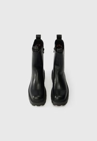 Crne gležnjače od glatke kože s teksturiranim, debelim gumenim potplatom i trakama na zadnjem dijelu za lakše obuvanje. Unutrašnjost je obložena leopardskim uzorkom.