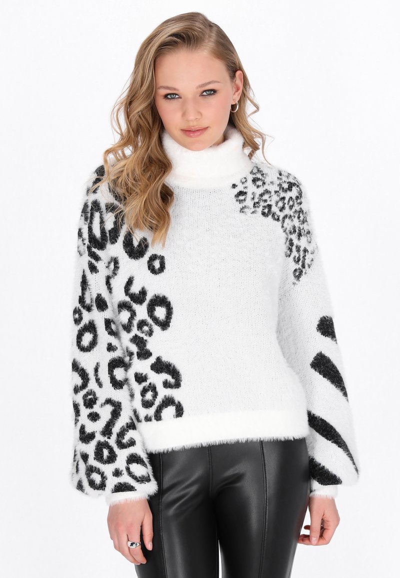 Pulover fuzzy alb-negru cu guler înalt, având un imprimeu leopard variat și mâneci supradimensionate, asortat cu pantaloni negri strâmți.