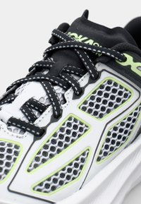 White mesh running shoe featuring black and lime green accents, with a textured overlay and contrasting laces. Breathable design.