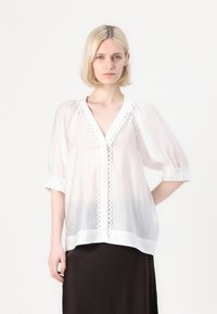 Blusa bianca trasparente con scollo a V profondo, maniche a palloncino corte e dettagli decorativi con bottoni lungo la parte anteriore. Dettagli arricciati sulle maniche.