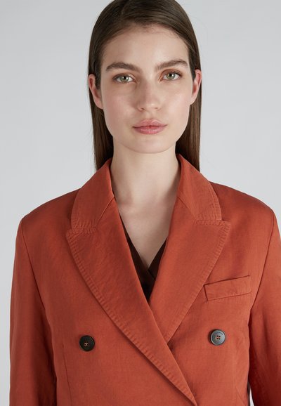 Blazer de doble botonadura de color óxido con cuello muesca, dos botones y un bolsillo en el lado izquierdo. Textura suave.