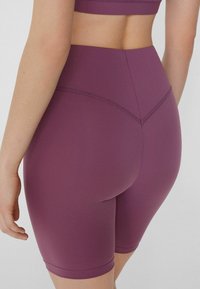 Shorts da ciclismo a vita alta, aderenti, di un profondo viola prugna, realizzati in tessuto elastico con texture liscia e dettagli di cuciture piatte.