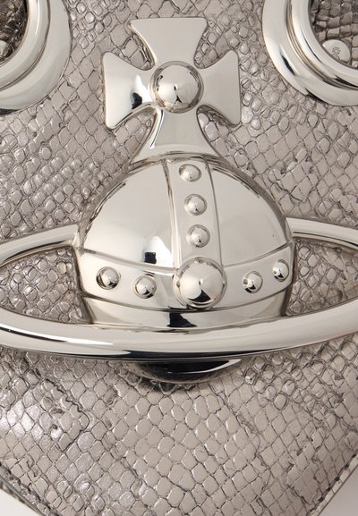 Λείο ασημένιο έμβλημα σε σχήμα σφαίρας με καρφιά και σταυρό πάνω σε υφή γκρίζας φίδιου δέρματος, μέρος αξεσουάρ μόδας.