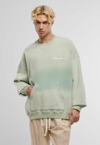 Sweatshirt verde cu un gradient, fabricat din bumbac, având un buzunar tip cangur. Imprimare distinctivă „ANOTHER COTTON” pe piept. Textură moale.