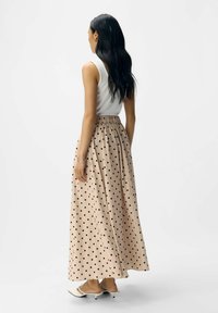Falda larga hecha de una tela suave y ligera, con una cintura alta, color beige con lunares negros y un diseño fluido.