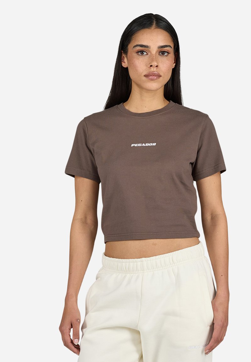 Maglietta cropped marrone con maniche corte e scollatura rotonda, con testo del marchio bianco al centro. Il materiale sembra morbido e liscio.