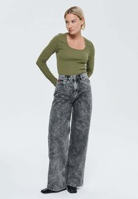 Haut à manches longues olive avec un décolleté carré, associé à un jean en denim gris taille haute et jambes larges, présentant une finition délavée et des coutures contrastantes.