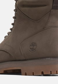 Primo piano di un boot impermeabile in pelle marrone con dettagli cuciti e suola in gomma a tasselli.