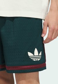 Green mesh shorts with perforations, featuring a white Adidas logo on the lower left, accented by a maroon stripe along the hem.