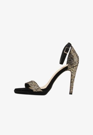Czarne aksamitne sandały na wysokim obcasie z biżuteryjnym akcentem na pasku, otwarty czubek i zapinany pasek na kostce, o smukłym, spiczastym kształcie.
