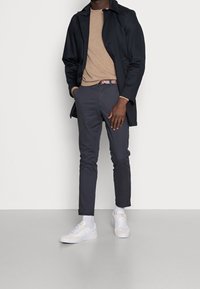 Tmavě námořnický kabát, světle hnědý svetr, tmavě šedé kalhoty a bílé tenisky. Oblečení doplňuje hnědý pásek a ohrnuté lemy kalhot.