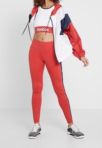 Röda träningstights kombinerade med en vit crop top och en färgblockerad jacka i vitt, rött och marinblått. Grå träningisskor fulländar outfiten.