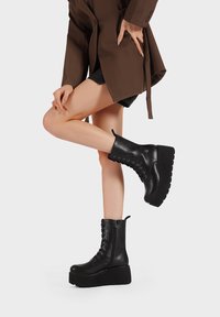 Botas de tobillo de imitación de cuero negro con plataforma gruesa, cordones en la parte delantera y cremallera lateral. Presenta puntera redonda y suela texturizada para mayor agarre.