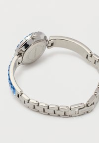 Ασημένιο μεταλλικό ρολόι βραχιόλι με διακοσμητικά από μπλε κρύσταλλο, ανοιχτό κούμπωμα και χαραγμένη υπογραφή Swarovski στο πίσω μέρος και το κούμπωμα.