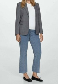 Blazer de rayas grises sobre una camisa blanca, combinado con jeans acampanados de color azul claro y zapatos negros. El blazer presenta solapas con muescas y bolsillos.