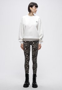 Balta sporta džemperis ar noslīpētām pleciem un logotipu, kombinēts ar leoparda raksta legingiem un melniem šņorzābakiem. Gluda auduma tekstūra.