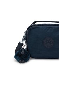 Borsa Kipling blu navy con chiusura a zip, materiale tessile, patch rotondo con logo e un accessorio portachiavi a forma di scimmia pelosa sulla tracolla.