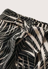 Tissu noir et blanc avec des motifs de feuilles abstraits, doté d'une ceinture élastique froncée et d'une ceinture en tissu nouée.