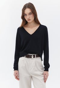 Suéter de cuello en V en navy hecho de un material de punto suave, combinado con pantalones beige y un cinturón marrón con hebilla plateada. Corte casual, mangas largas.