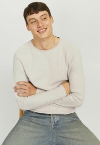 Hellgrauer, langärmliger, strukturierter Pullover mit Rundhalsausschnitt, kombiniert mit blauen Jeans aus Denim, die einen lässigen Schnitt und umgeschlagene Ärmel haben.