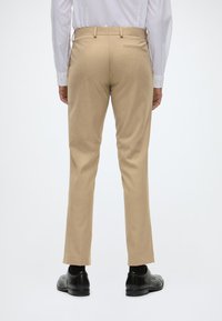 Pantaloni bej cu croi ajustat, textură netedă, design cu picior drept și detaliu de buzunar la spate, asortați cu pantofi din piele negri.