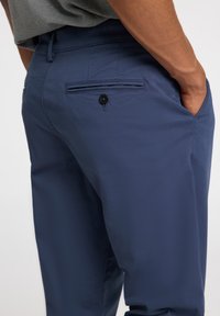 Marineblauwe broek van gladde stof, uitgerust met een achterzak met knoopsluiting en een slim fit ontwerp.
