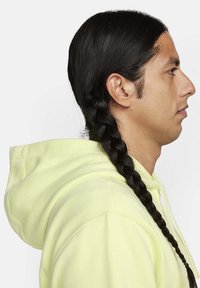 Felpa gialla brillante con tasca frontale, mostrata di lato. Presenta una lunga acconciatura nera intrecciata. La texture del tessuto è visibile e liscia.