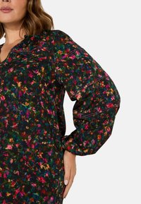 Šaty s květinovým potiskem a dlouhými balónovými rukávy v mnohobarevném materiálu na černém pozadí. Mají výstřih do V a jemné švy.