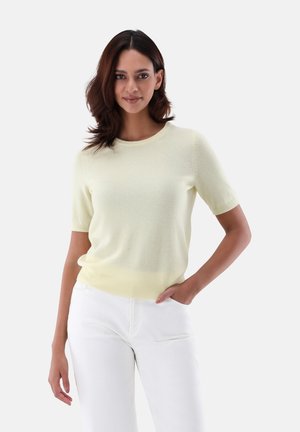 Light yellow short-sleeve knit sweater with a round neckline and ribbed hem; worn with white pants, smooth texture, no visible patterns.