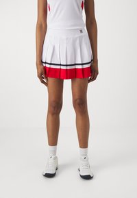 White pleated skirt with red and black stripes, made of lightweight fabric. Paired with white athletic shoes and socks.