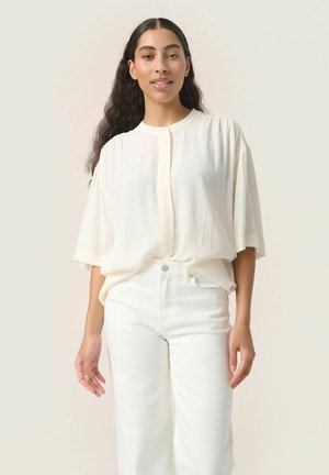Blusa crema a maniche corte con scollatura rotonda. Tessuto leggero e strutturato che cade dolcemente. Abbinata a jeans bianchi a vita alta.