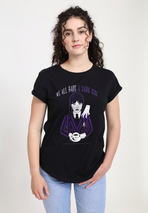 Young woman with curly hair wears black T-shirt showing a dark-haired girl in striped outfit holding a coffee cup under a disembodied hand, text above.