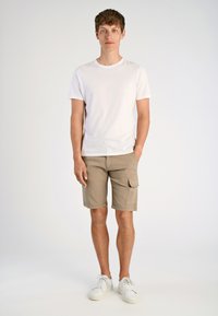 Biały t-shirt z okrągłym dekoltem w połączeniu z khaki szortami cargo z bocznymi kieszeniami i luźnym krojem, uzupełnione białymi trampkami.