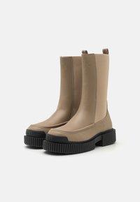 Stivali ankle beige con una finitura liscia e opaca e suola in gomma testurizzata. Presentano un'etichetta per il pull, lati elastici e logo in rilievo sulla punta.