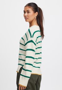 Maglione a righe in crema e verde, con scollo rotondo, spacchi laterali e orlo a contrasto color senape. Texture a maglia morbida, vestibilità rilassata.