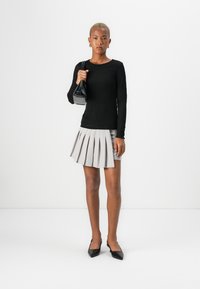 Top negro texturizado de manga larga combinado con una mini falda plisada gris claro, tacones negros de punta y un pequeño bolso negro.