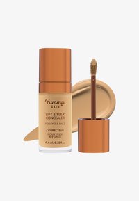 Corrector Yummy Skin Lift & Flex en un frasco de vidrio transparente con tapón dorado rosado. Viene con un aplicador en forma de pie de pato. Sombra de producto crema beige.