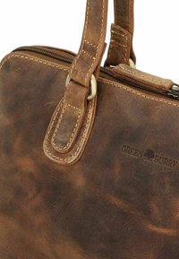 Borsa in pelle marrone con cuciture visibili, chiusura a zip e logo. Dispone di un manico singolo con un accessorio in metallo.