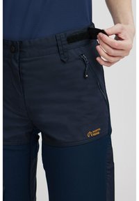 Mėlynos lauko kelnės su lygia tekstūra, elastinga juosmens juosta su Velcro, užtrauktukais užsegamos kišenės ir oranžiniu "NORTH BEND" logotipu šone.
