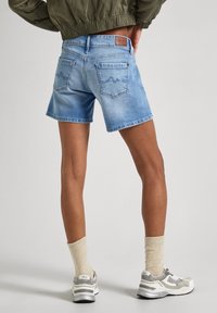 Shorts in denim blu chiaro con taglio dritto, cuciture visibili e due tasche posteriori. Abbinati a sneakers grigie e bianche e calzini beige.